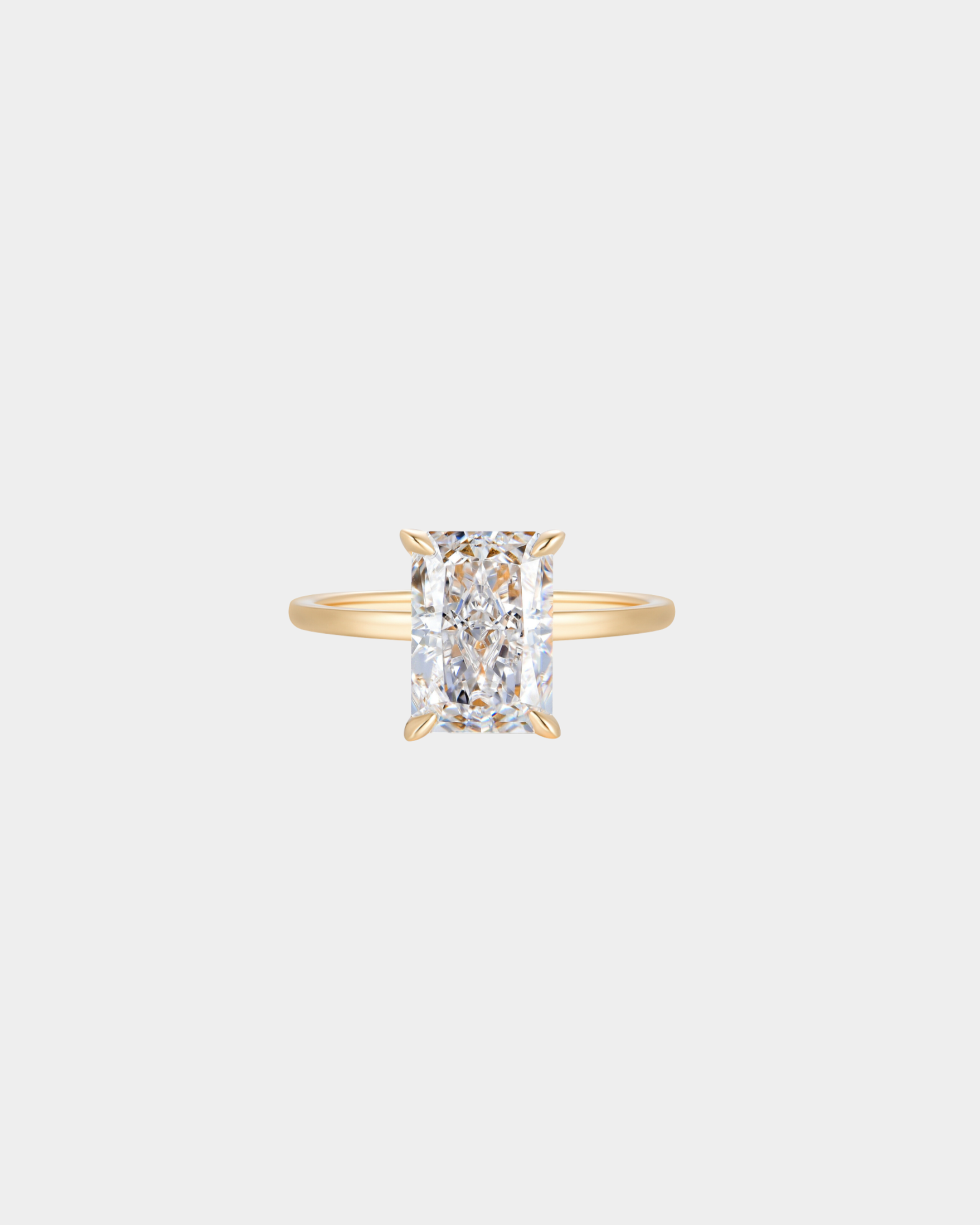 Gold ring with a rectangle shaped diamond looking centre stone on a light grey background