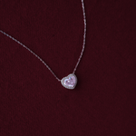 Heart-shaped pink gemstone necklace on a chain against a dark red background