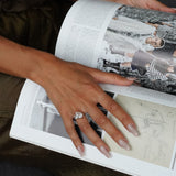 Person holding an open book with a close-up of a hand wearing an aurora ring on a dark surface.