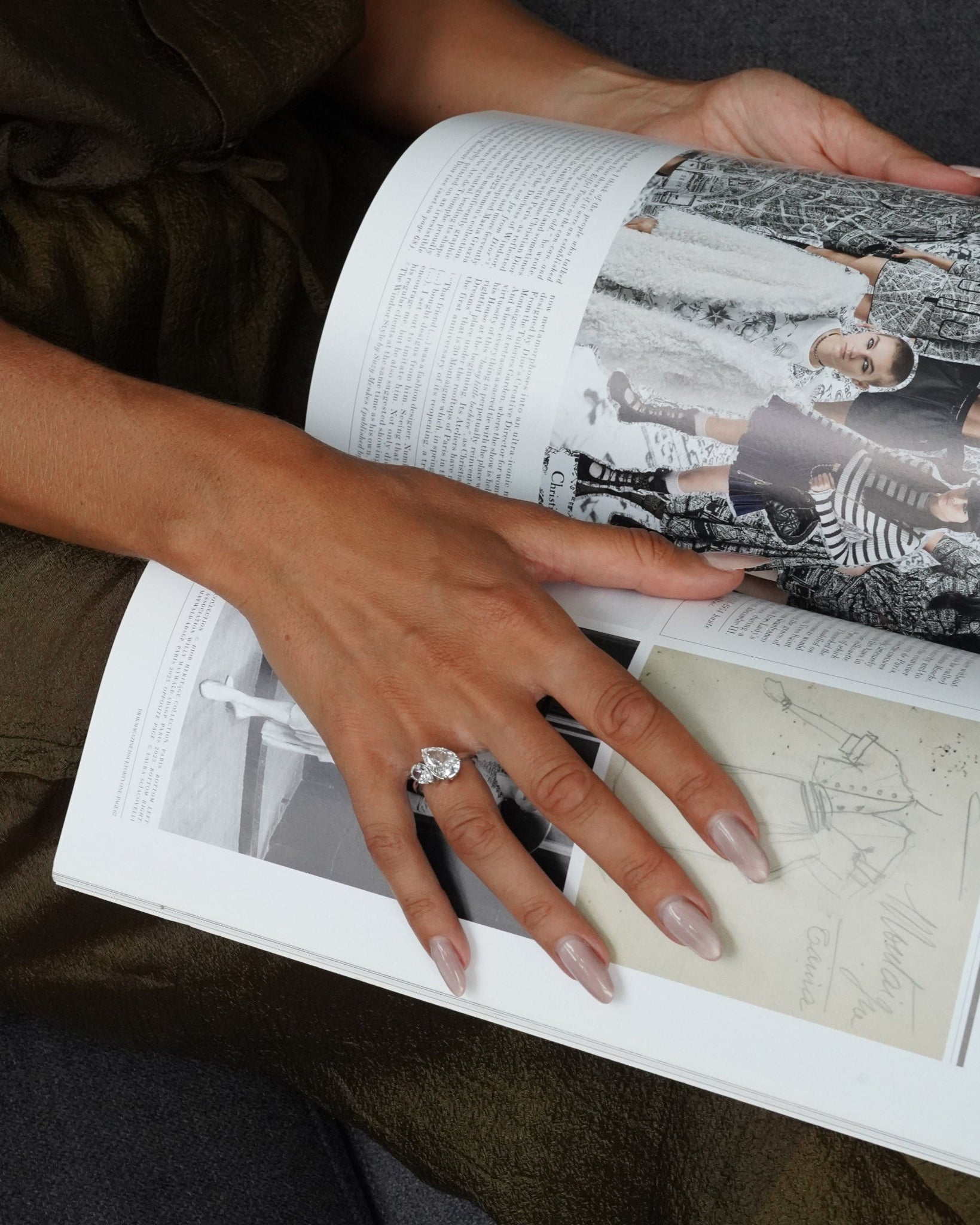 Person holding an open book with a close-up of a hand wearing an aurora ring on a dark surface.
