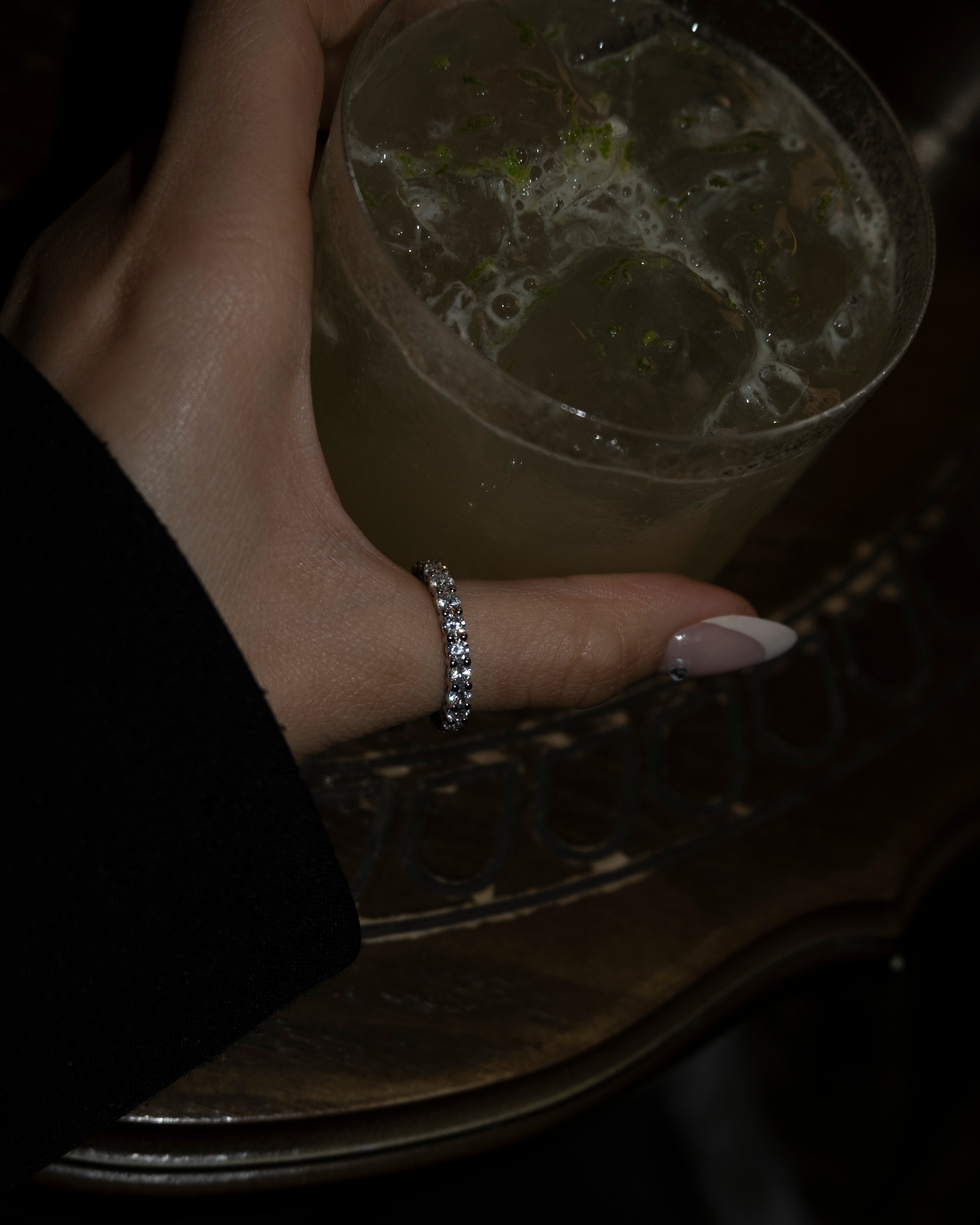 Hand holding a drink with a ring on a dark surface