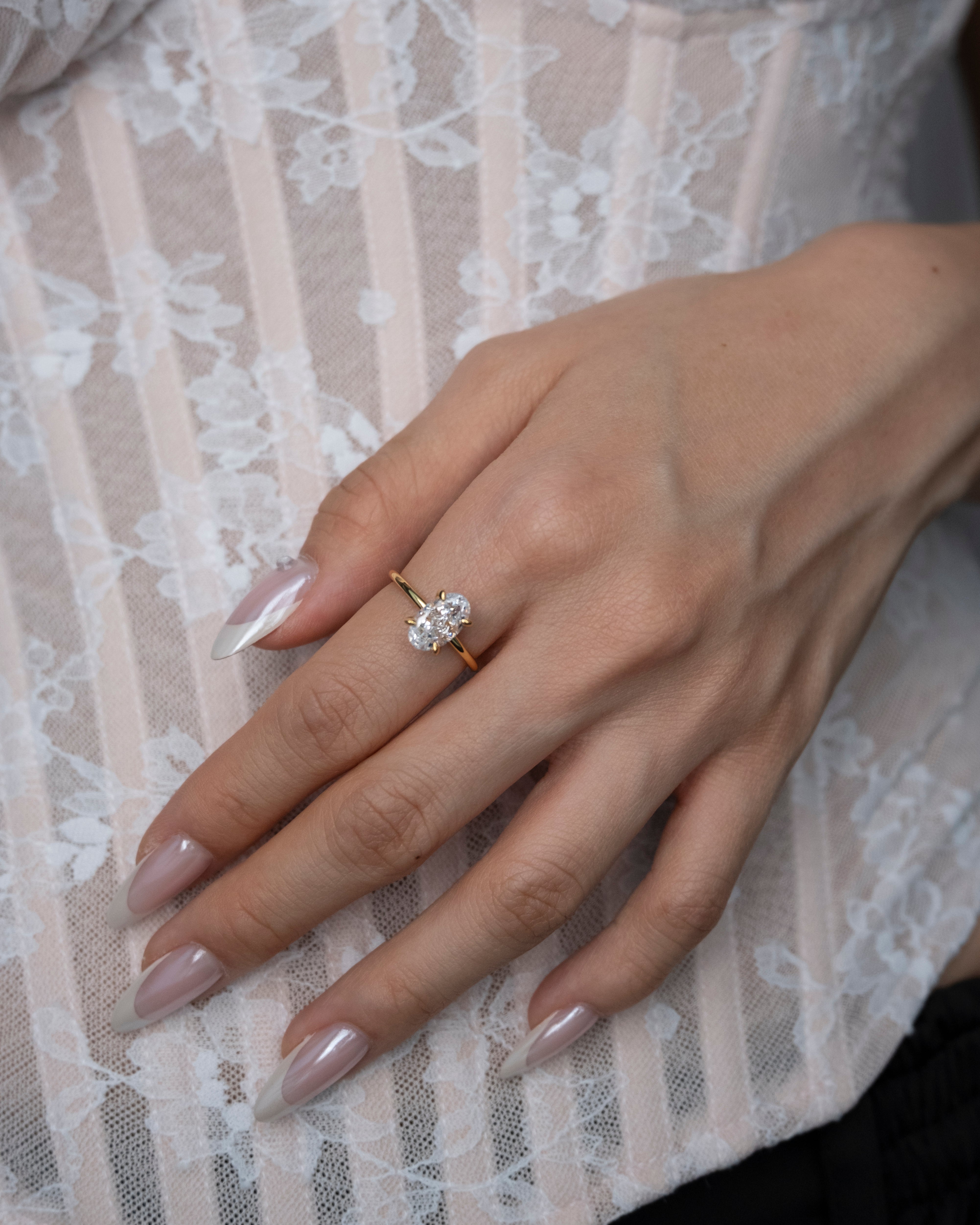 Hand wearing a diamond ring on a lace fabric background