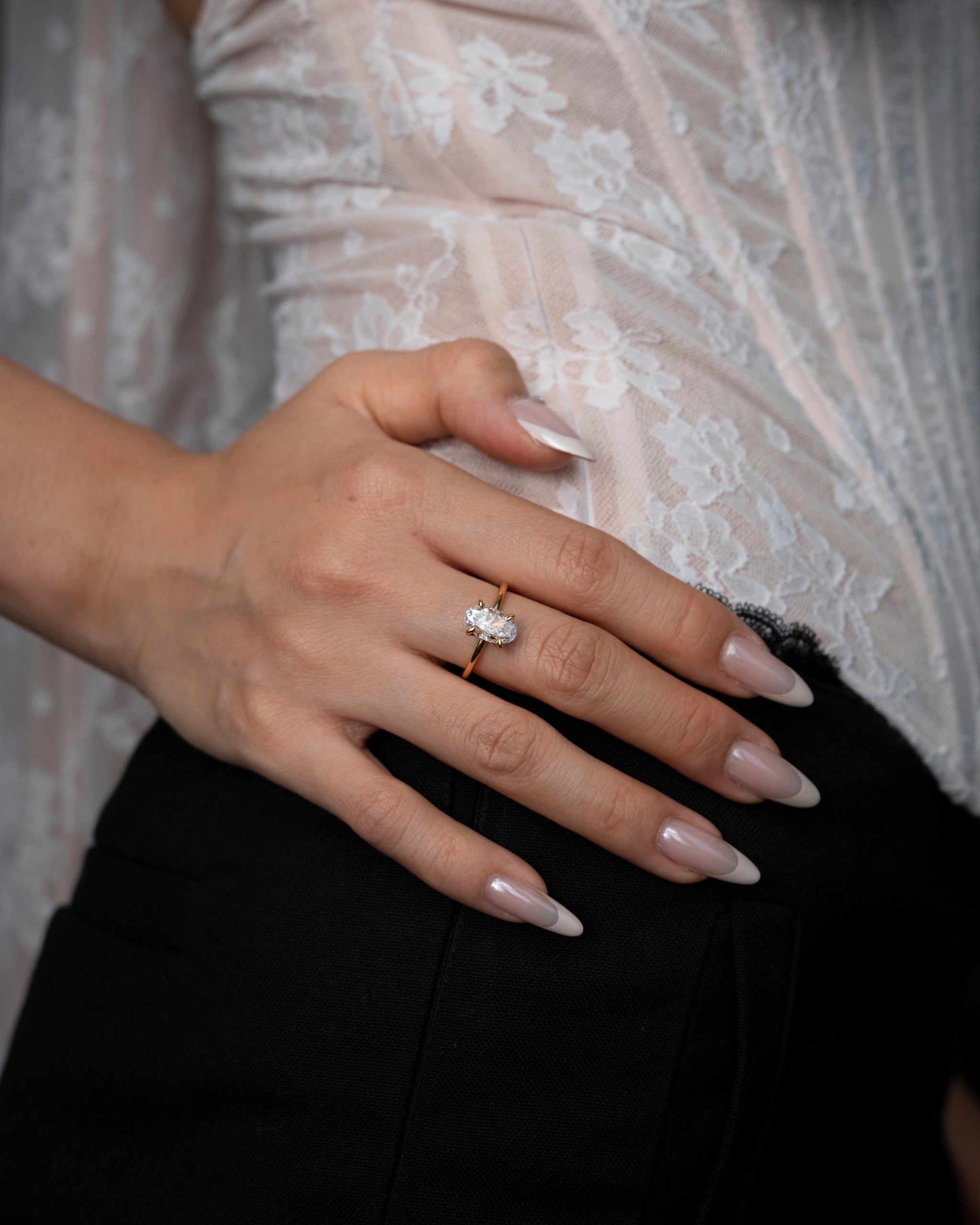 Hand wearing a diamond ring with a blurred lace garment in the background