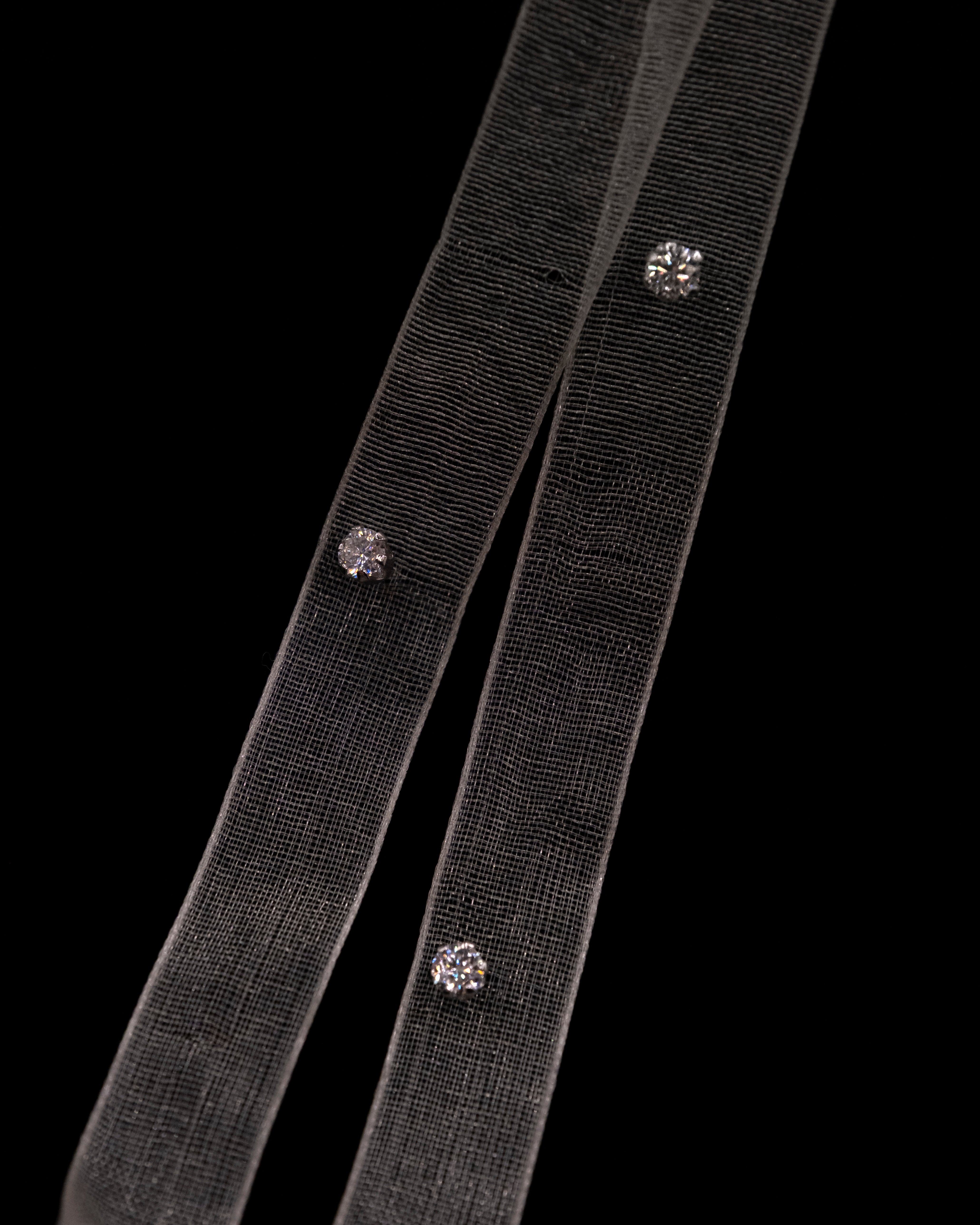 Two black ribbons with LUME's Stella studs on a clear background