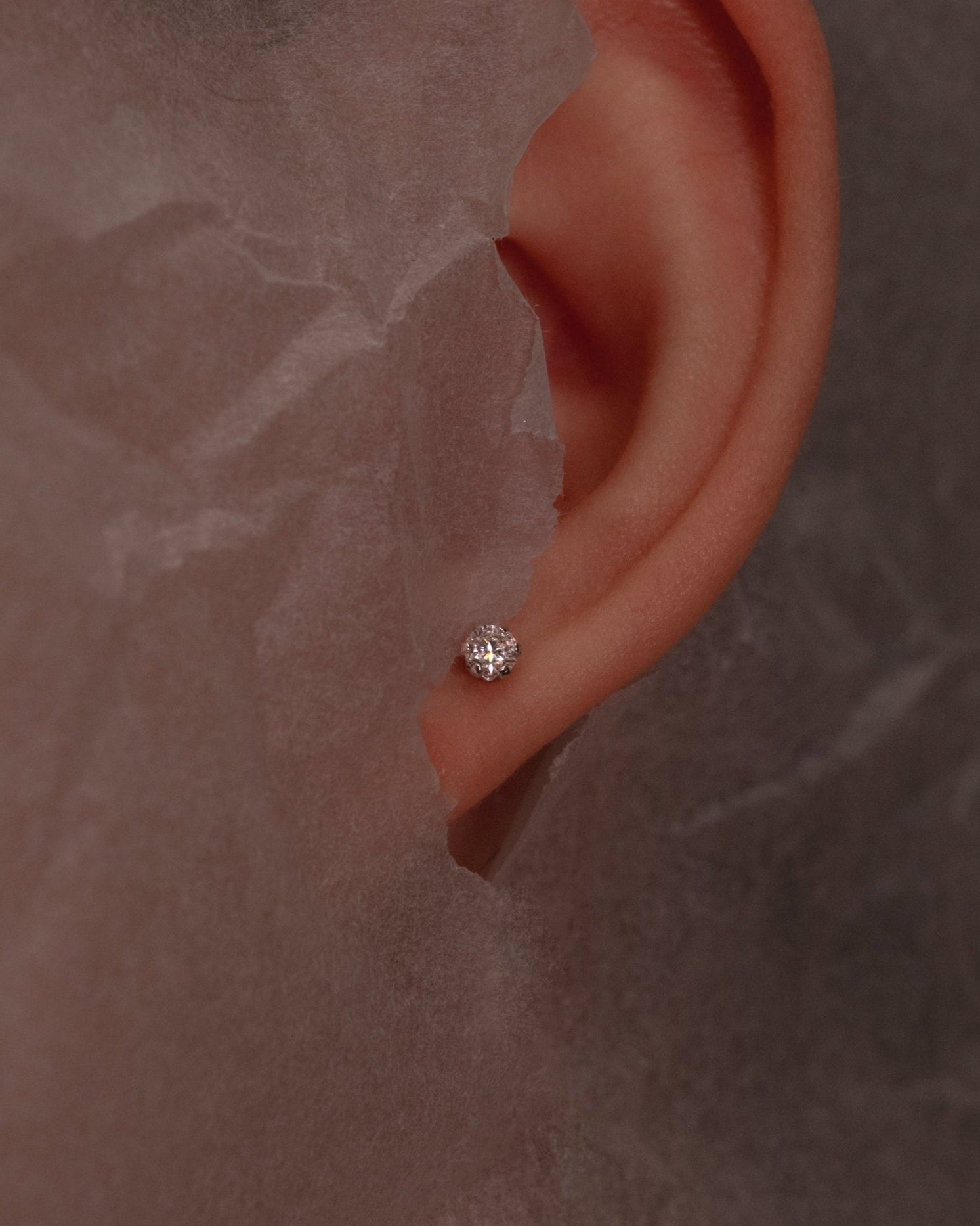 Close-up of an ear with a Mossanaite stud on a textured brown beige background