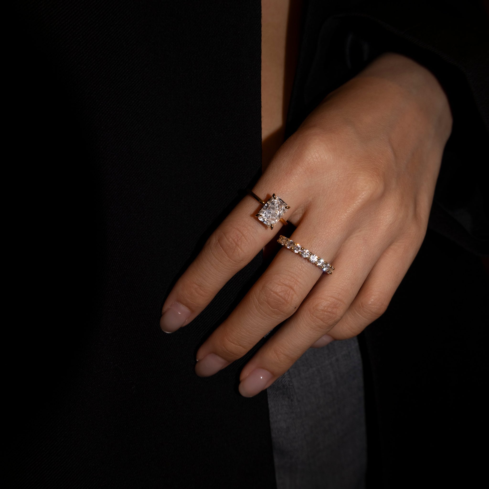 Close-up of a hand wearing lume jewellery's elodie ring and dues ring both in gold on a dark background