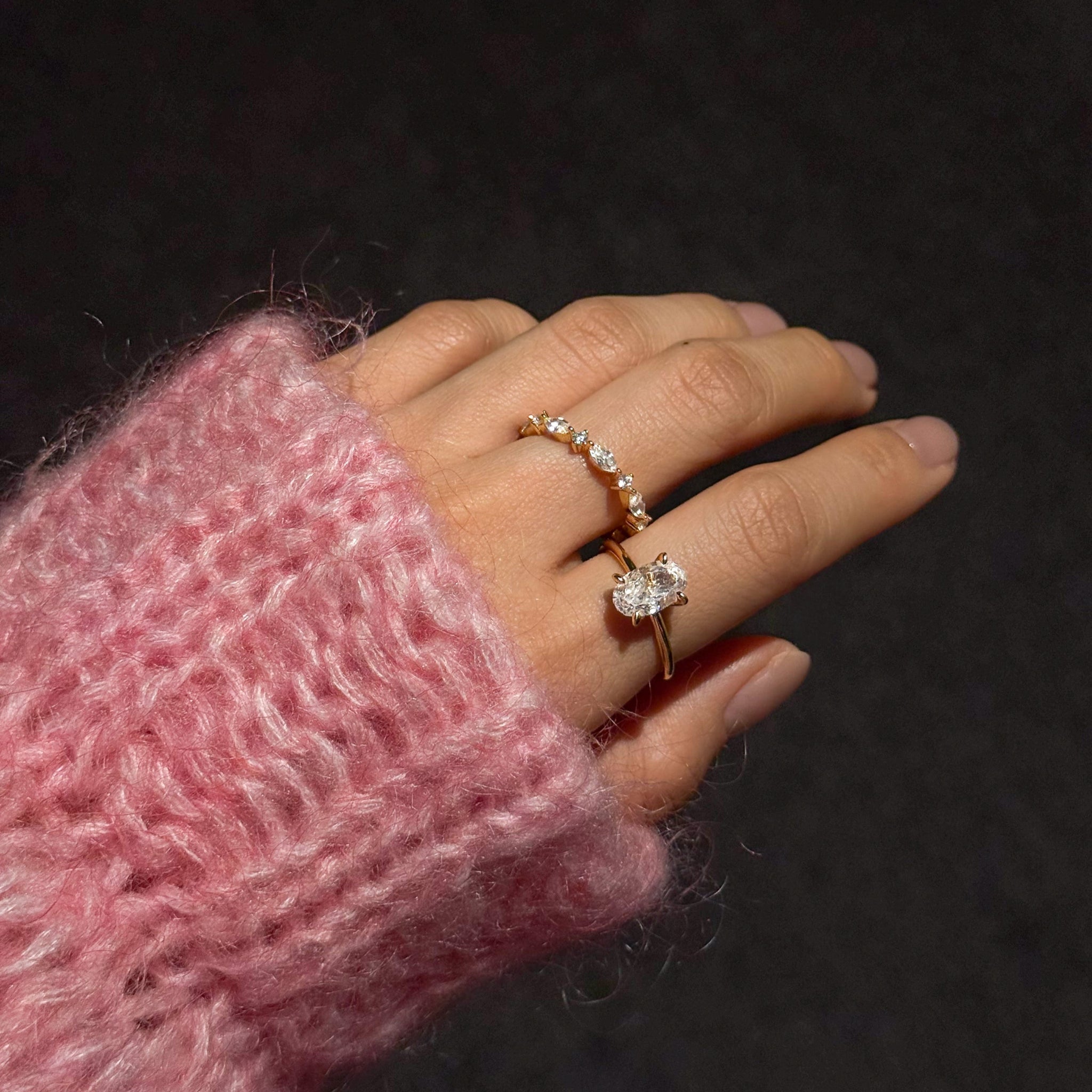 Hand wearing lume jewellery's celeste ring and ciel ring with a pink textured sleeve against a dark background