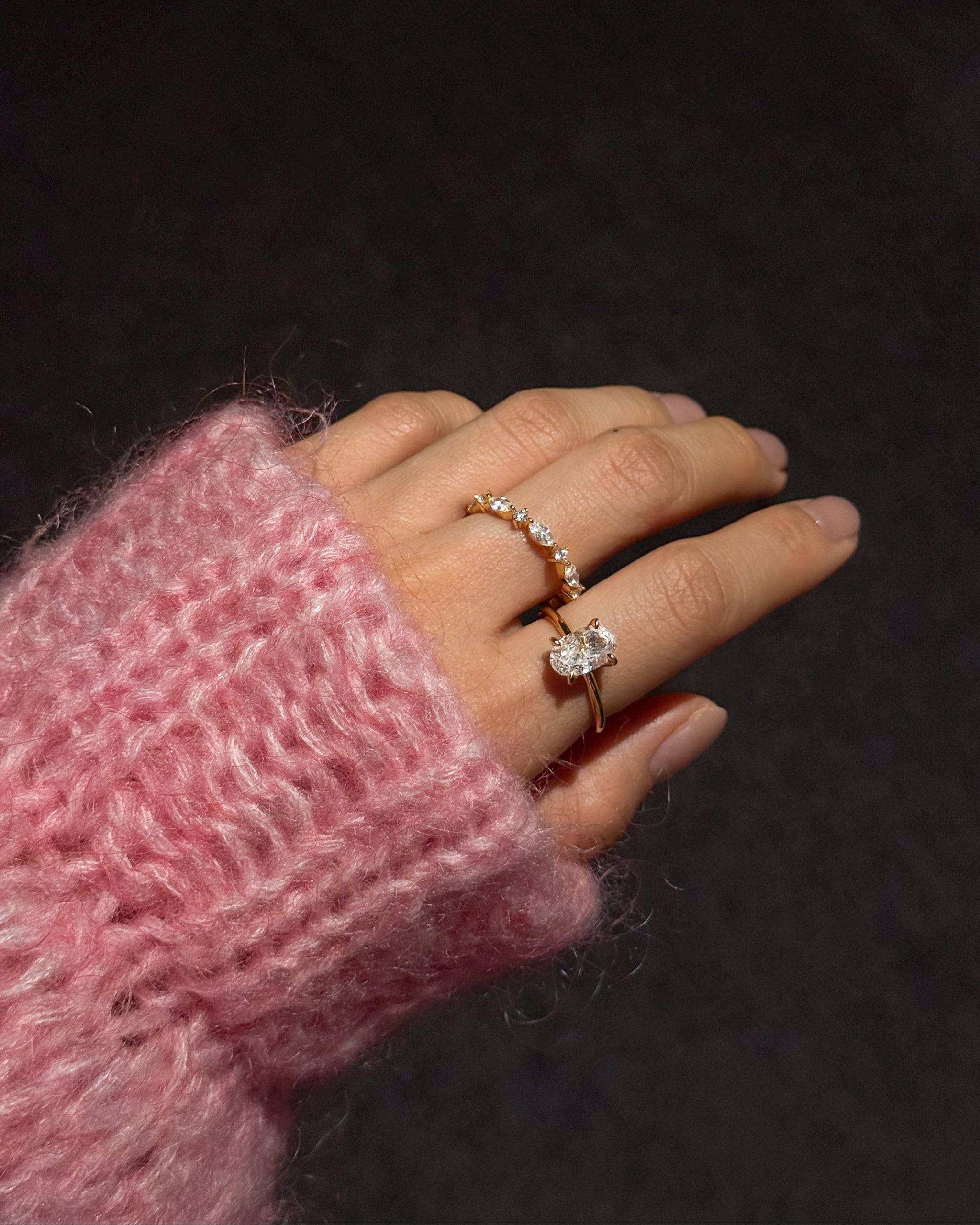 Hand wearing a diamond ring with a pink textured sleeve against a dark background