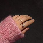 Hand wearing a ciel ring and a celeste ring with a pink sleeve against a dark background