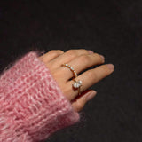 Hand wearing a ciel ring and a celeste ring with a pink sleeve against a dark background