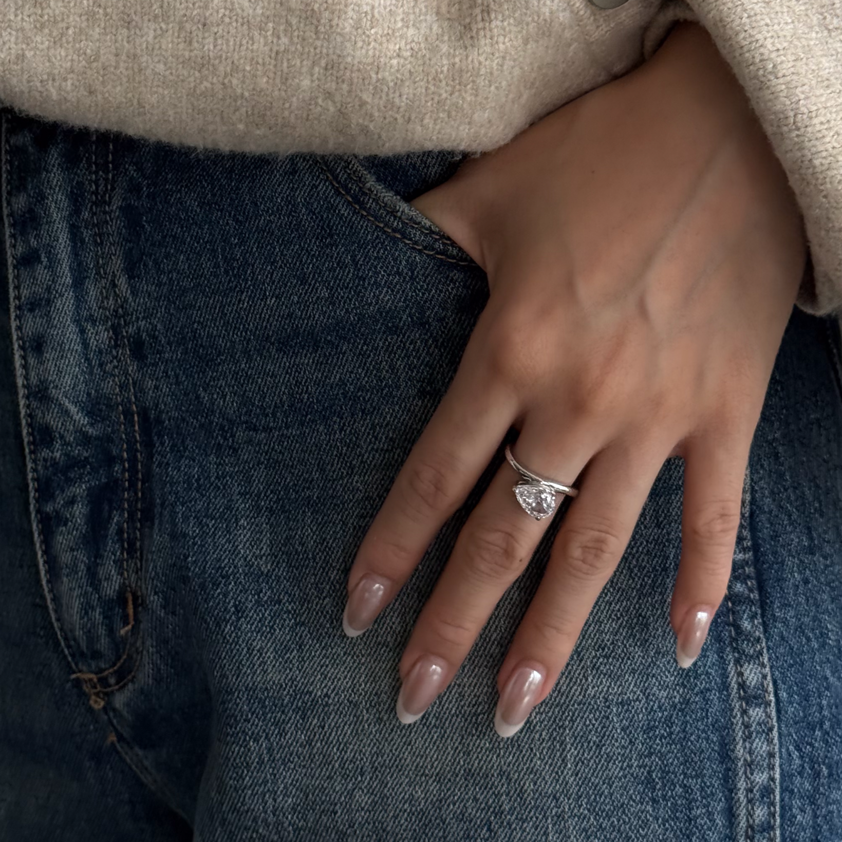 Close-up of a hand wearing lume's melora ring on blue jeans with a beige coat.