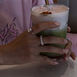 hands holding a drink wearing amore ring and roen ring from lume jewellery