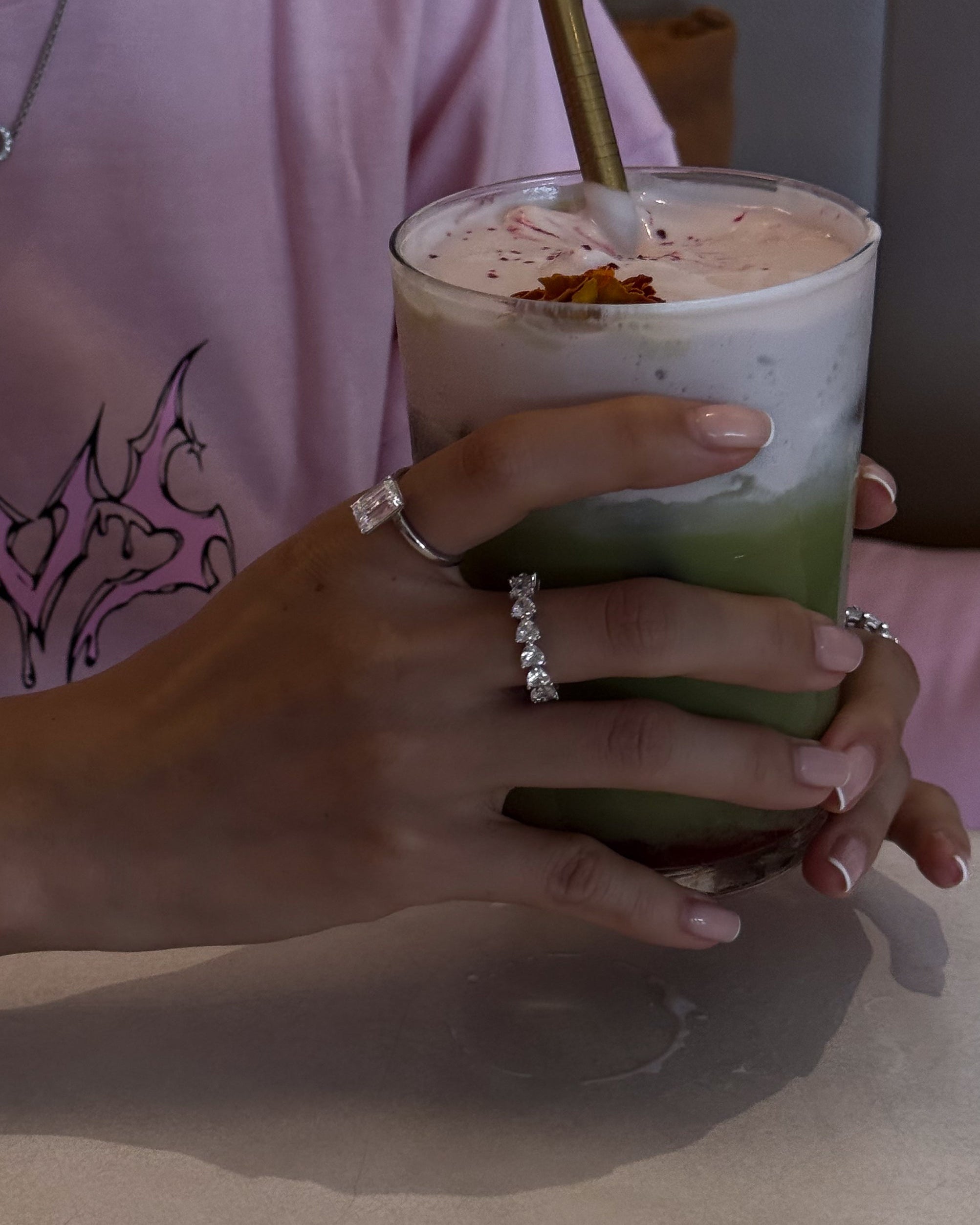 hands holding a drink wearing amore ring and roen ring from lume jewellery