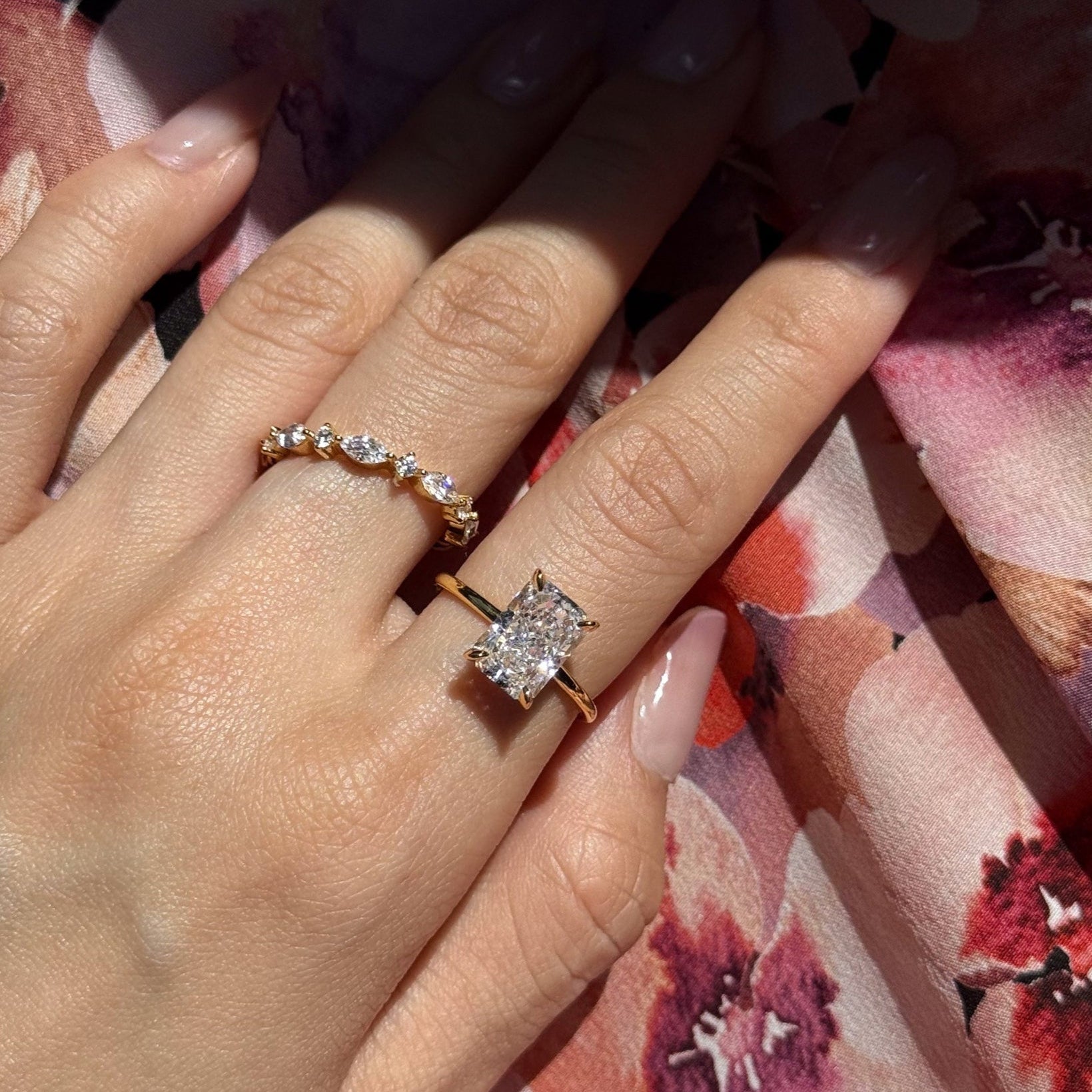 Close-up of a hand wearing lume jewelllery's celeste ring and elodie ring on a floral fabric background