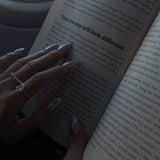 hand wearing lume jewellery's dues ring and ciel ring holding an open book.