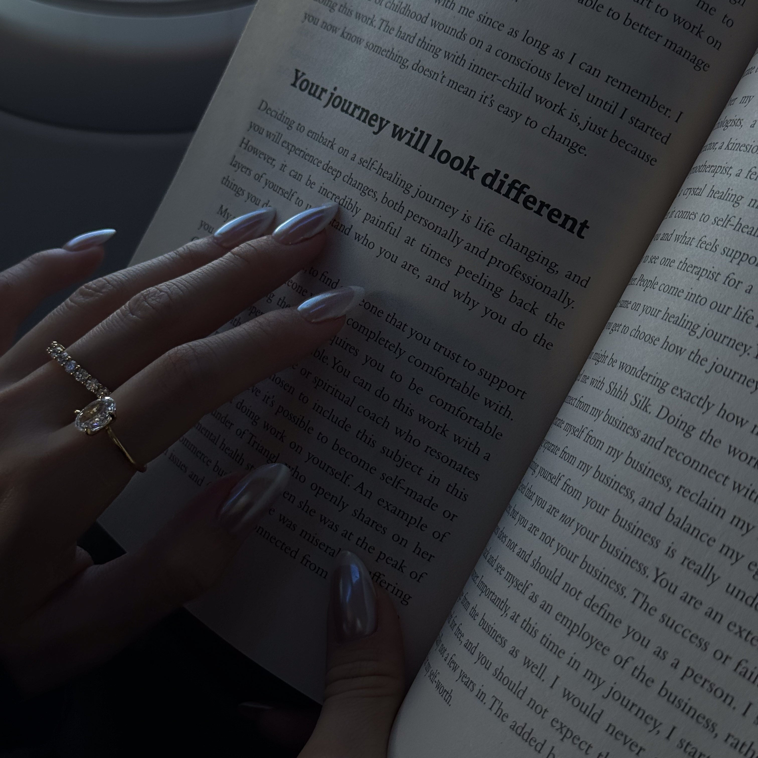 hand wearing lume jewellery's dues ring and ciel ring holding an open book.