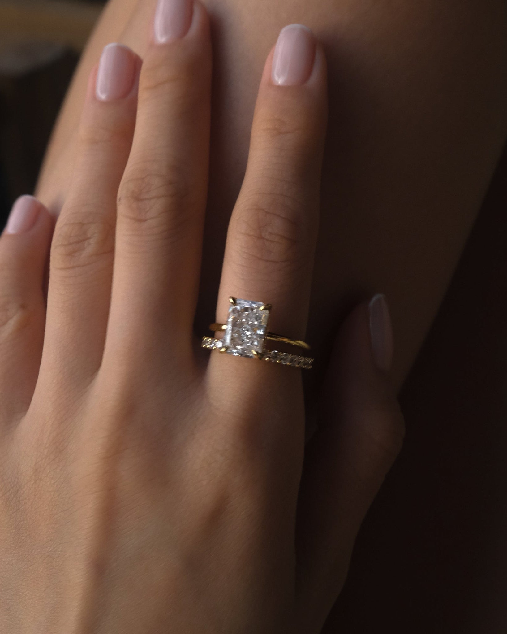 Close-up of a hand wearing a elodie ring and a dues ring on a dark background