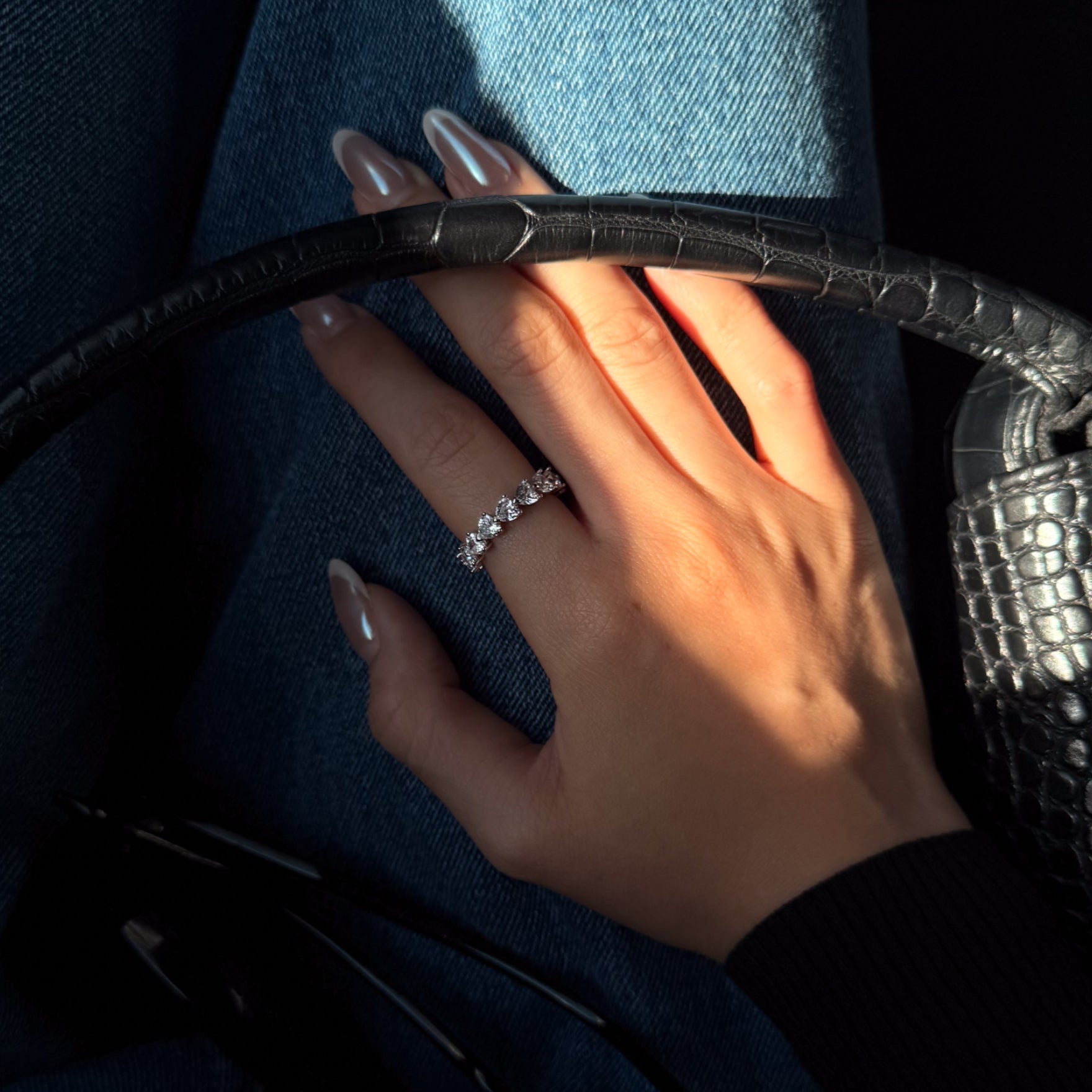 Hand with lume's amore ring holding onto a black crocodile-patterned handbag.