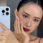 Woman holding a phone with a blurred background, hand wearing celeste ring