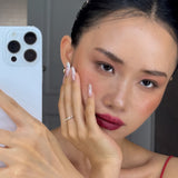 Woman holding a phone with a blurred background, hand wearing celeste ring