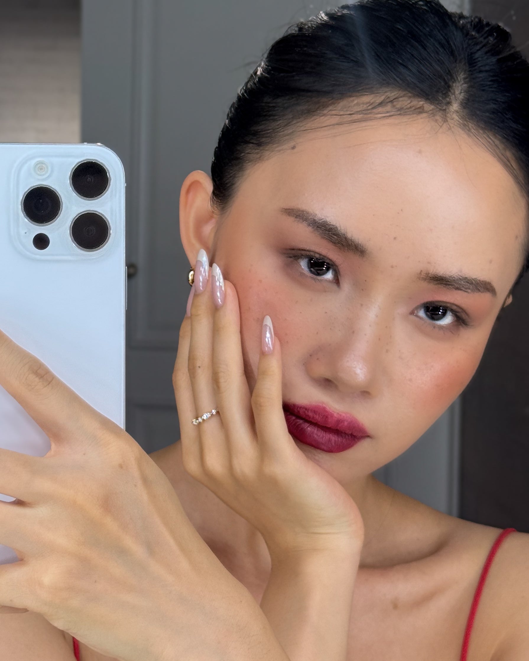 Woman holding a phone with a blurred background, hand wearing celeste ring
