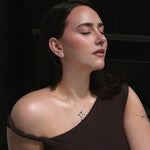 Woman wearing a brown one-shoulder top against a dark background, wearing the stella studs and silver necklace from lume jewellery