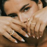 Woman with tattoos and wearing dues ring in gold and ciel ring on her fingers, holding her hands near her face.