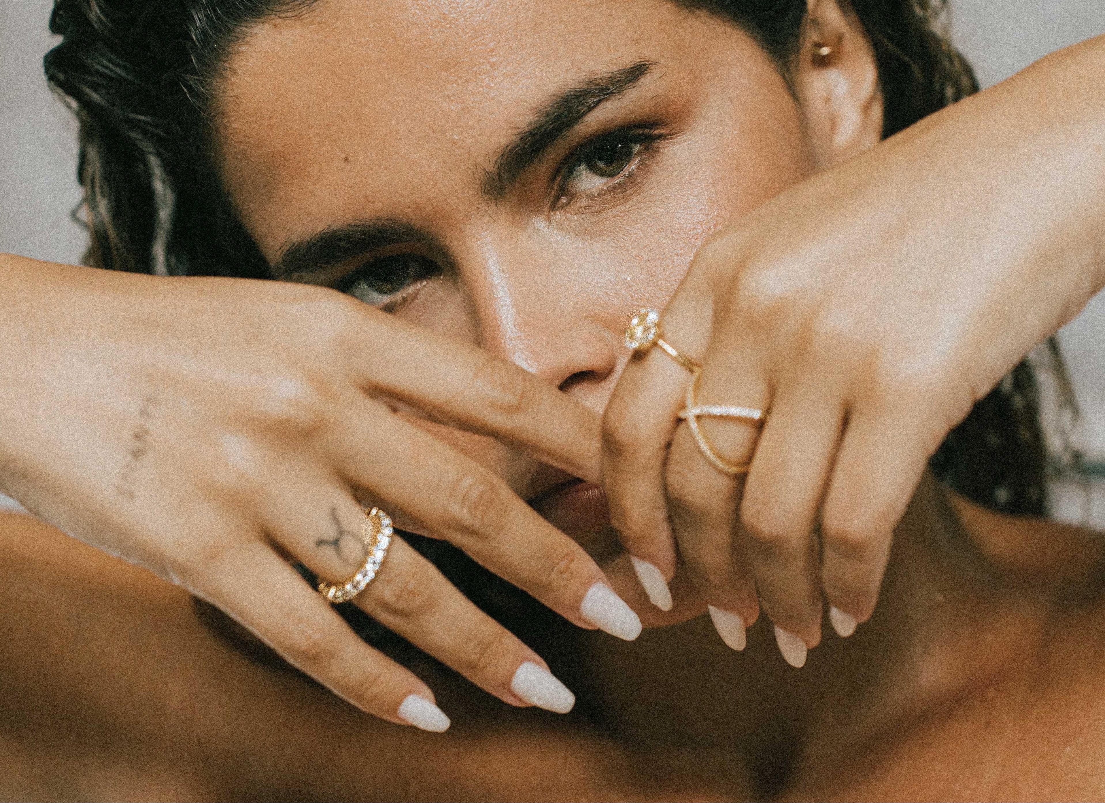 Woman with tattoos and wearing dues ring in gold and ciel ring on her fingers, holding her hands near her face.