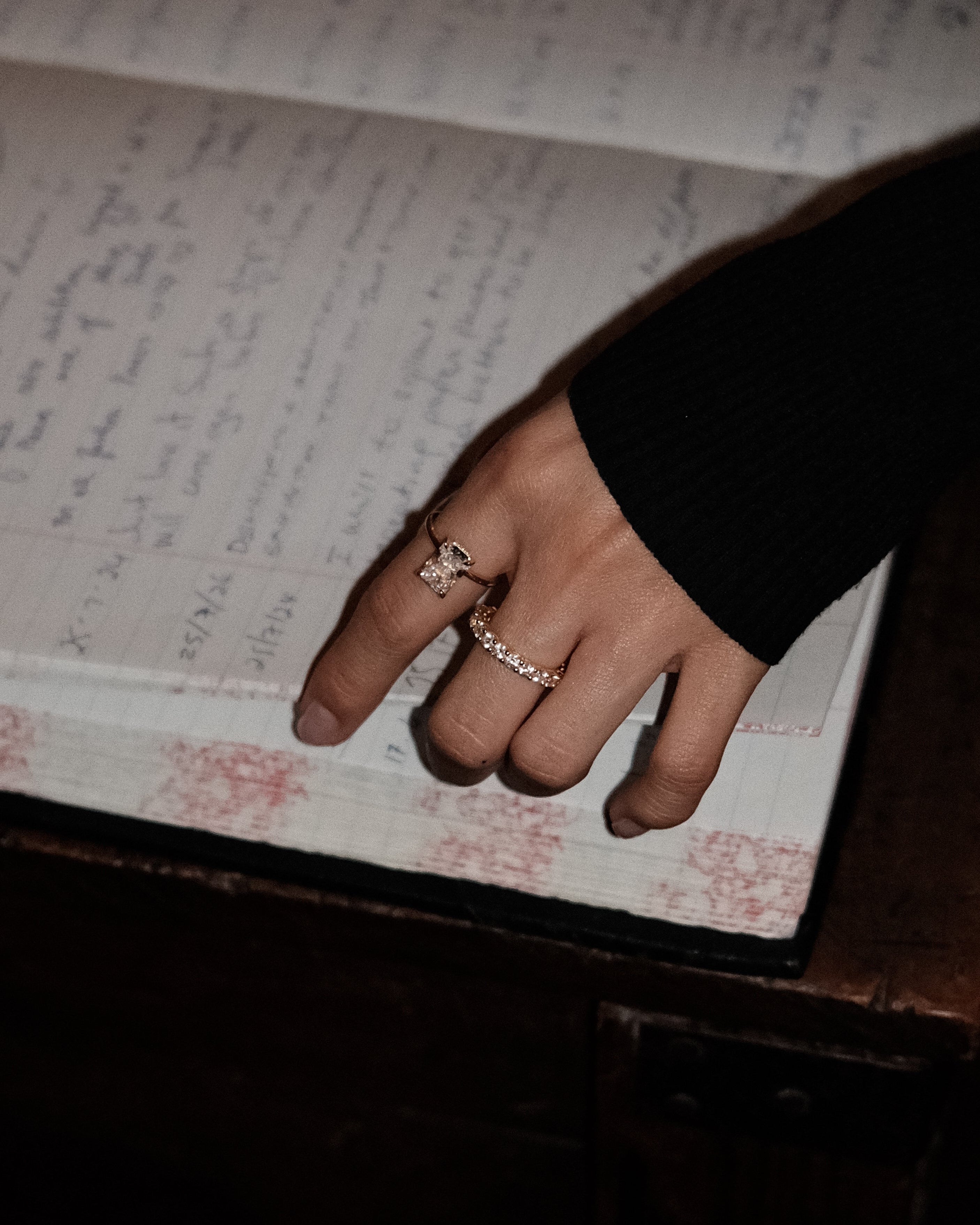 Hand with elodie ring and dues ring on an open book filled with handwritten text