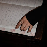 Hand with dues ring and elodie ring in gold on an open book filled with handwritten text