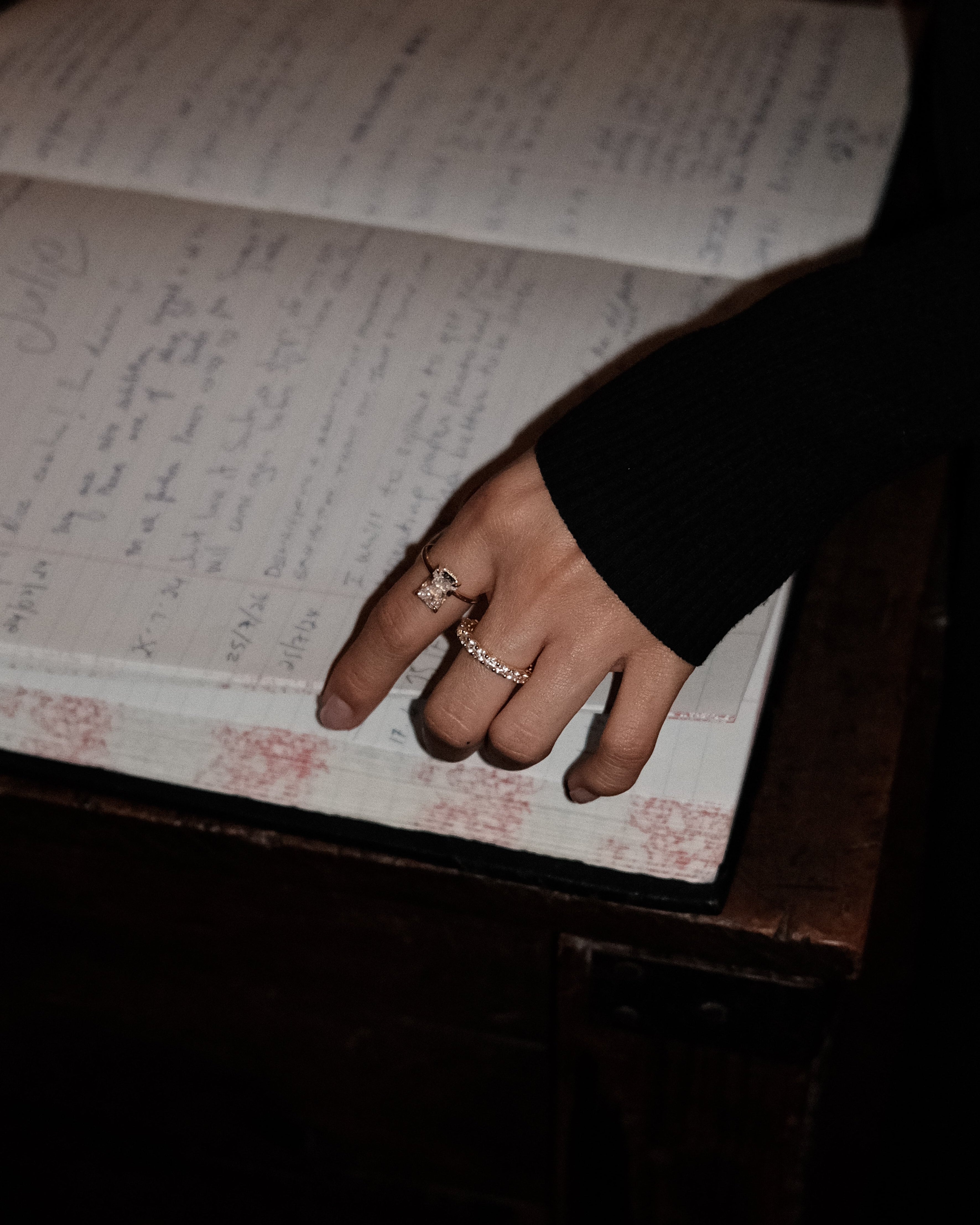 Hand with dues ring and elodie ring in gold on an open book filled with handwritten text