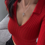 Person wearing a red ribbed sweater with a necklace featuring a heart and cross pendant.