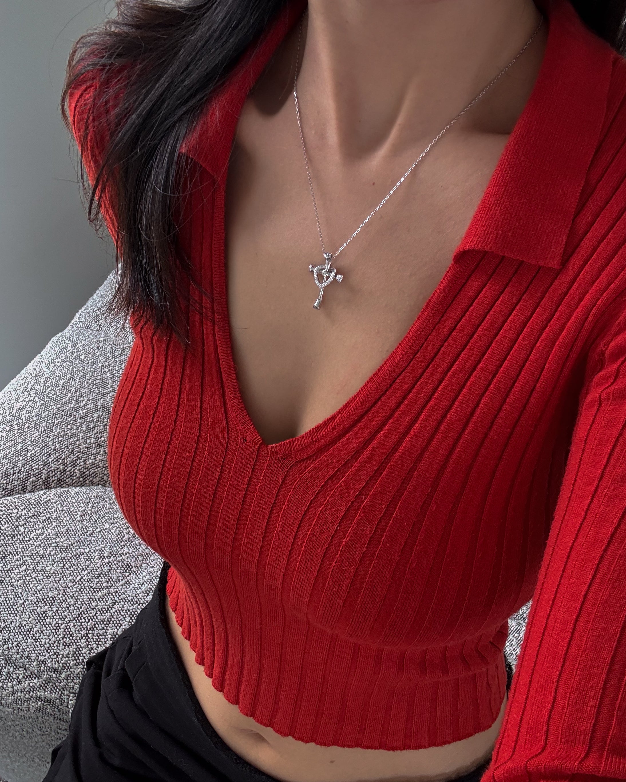 Person wearing a red ribbed sweater with a necklace featuring a heart and cross pendant.