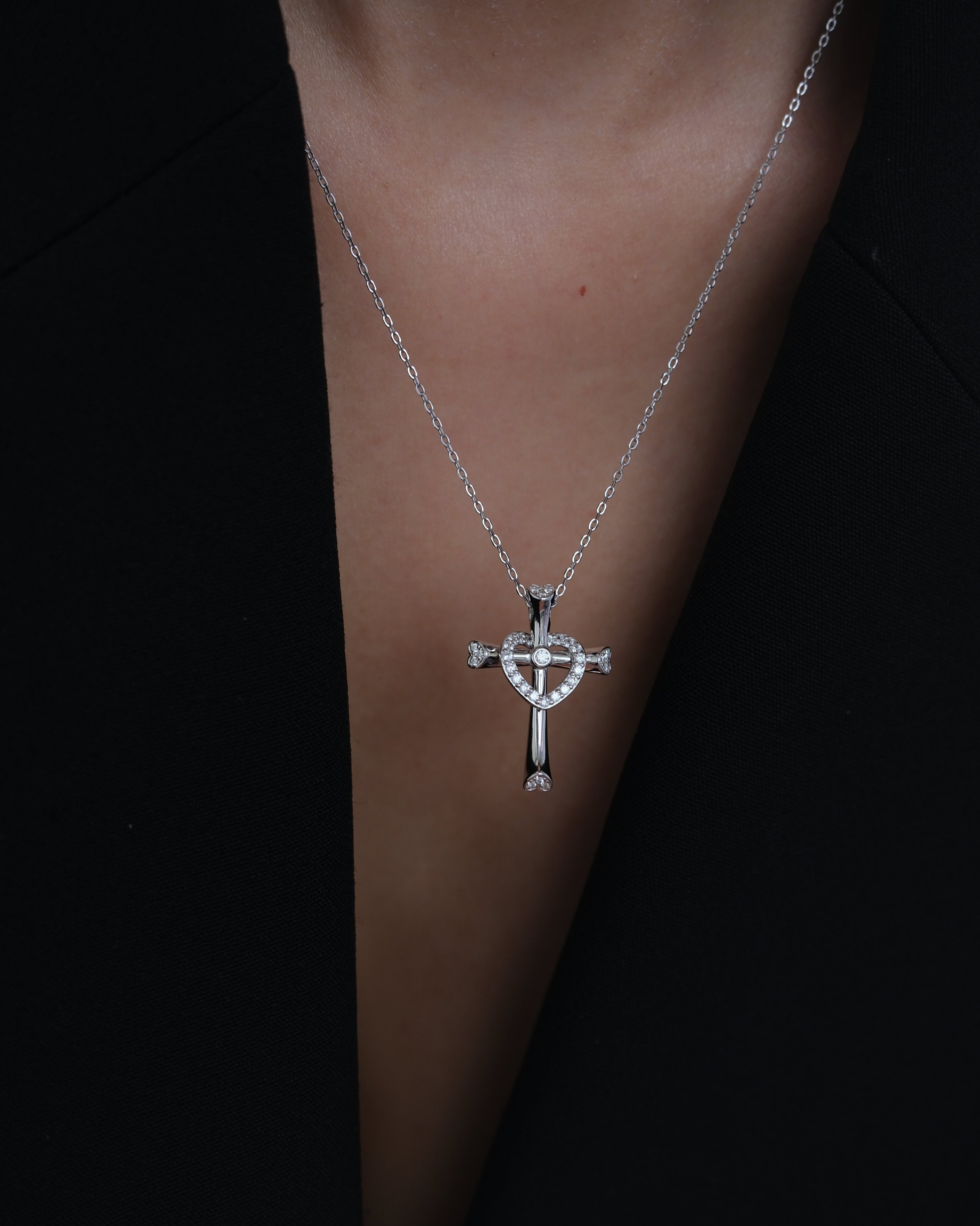 Silver necklace with a cross and heart pendant on a dark background