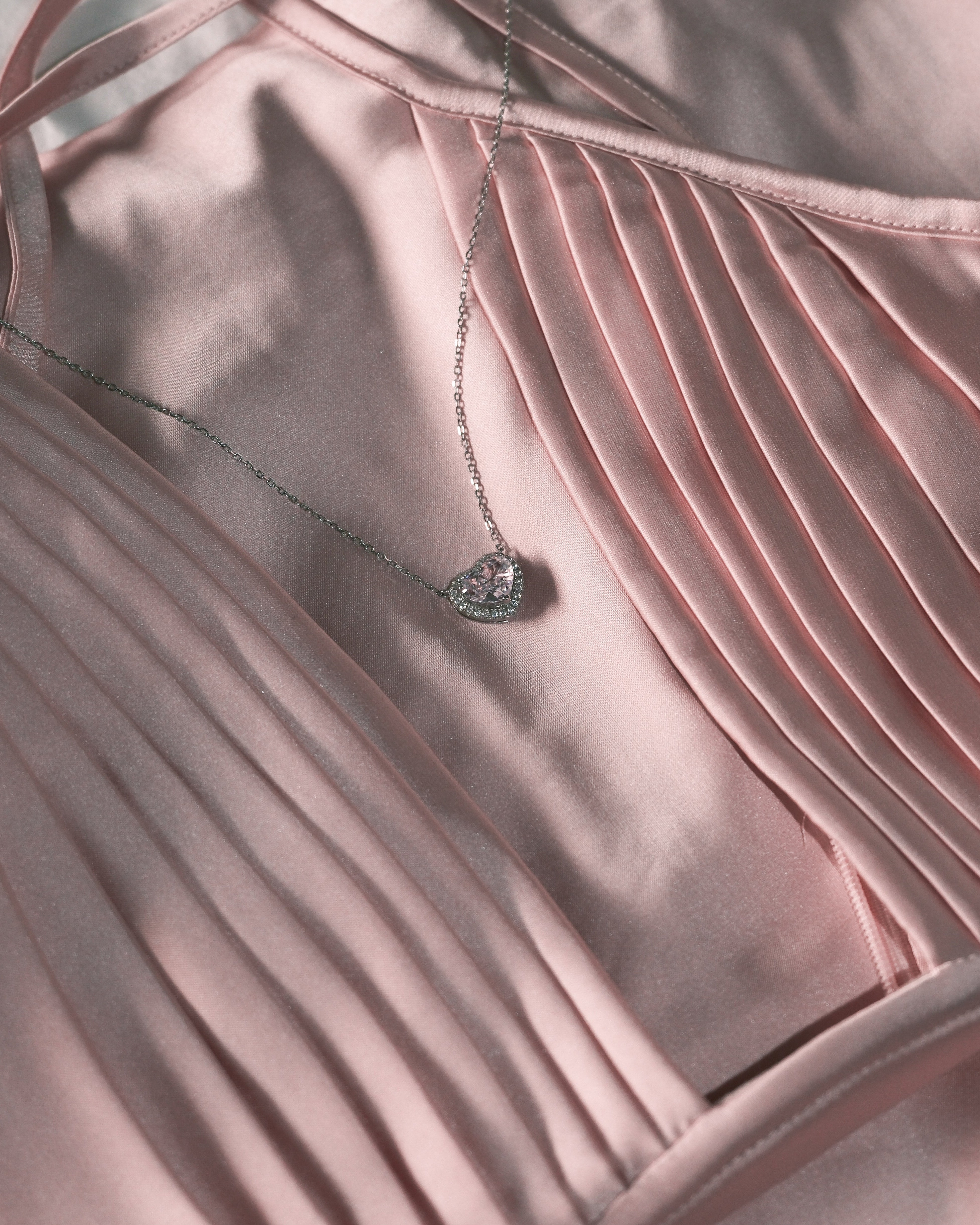 Necklace with a heart pendant on a pink satin fabric background