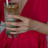 hand wearing gold selene ring holding a drink with a red dress on