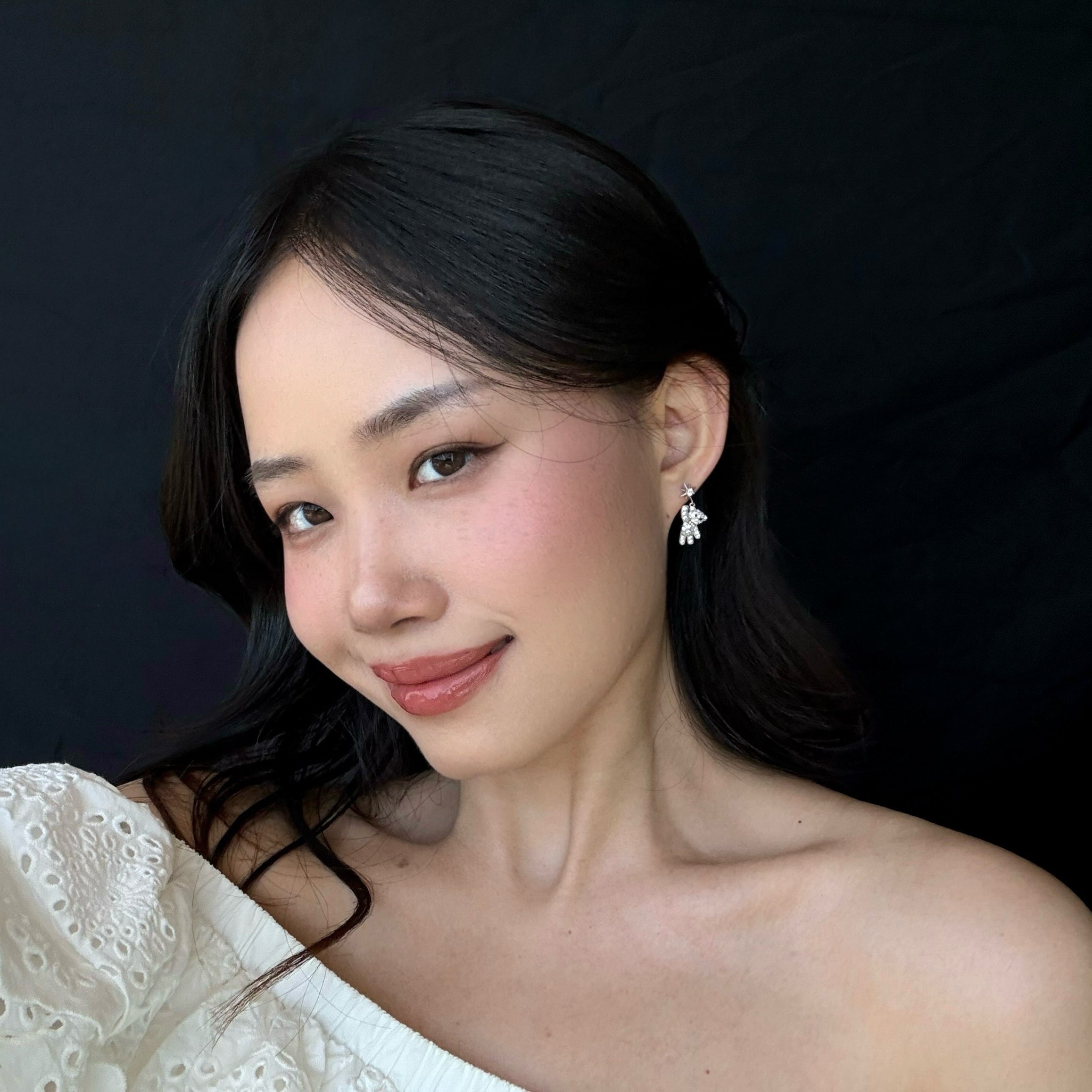 Woman wearing a white top and starry teddy earrings against a black background 